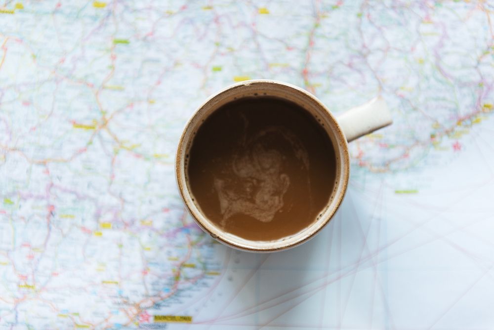 A coffee cup on a map, showing a journey. The coffee cup is centered, highlighting travel, exploration, and adventure.…