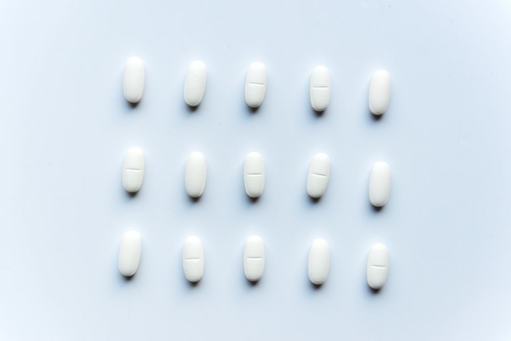 White pills arranged in a grid on a light background. Medication, pills, and tablets are evenly spaced. Pharmaceutical…