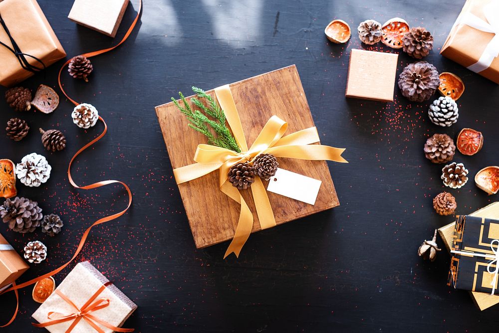 Festive gift box with pinecones and ribbon on a dark table. Holiday gift, wrapped gift, and decorative pinecones create a…