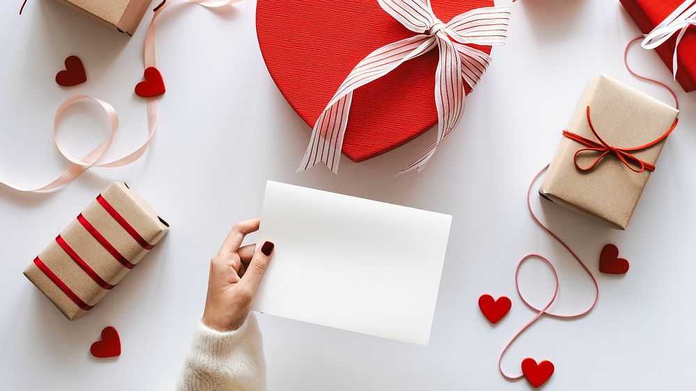 Gift boxes and a heart-shaped box with ribbons. A hand holds a blank card for Valentines or romantic occasions. Brown and…