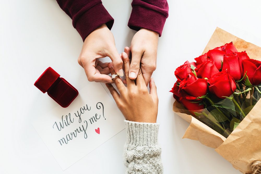 Hands exchanging a ring, a proposal with a ring box, and a note saying 'Will you marry me?' next to red roses. Romantic…