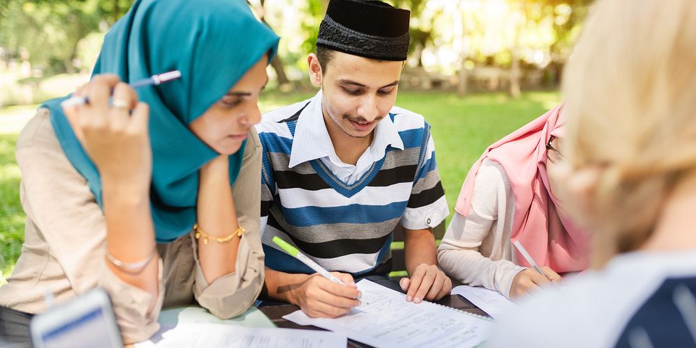 Group of young adults studying outdoors. Diverse students focus on notes. Collaborative learning in a park setting. Engaged…