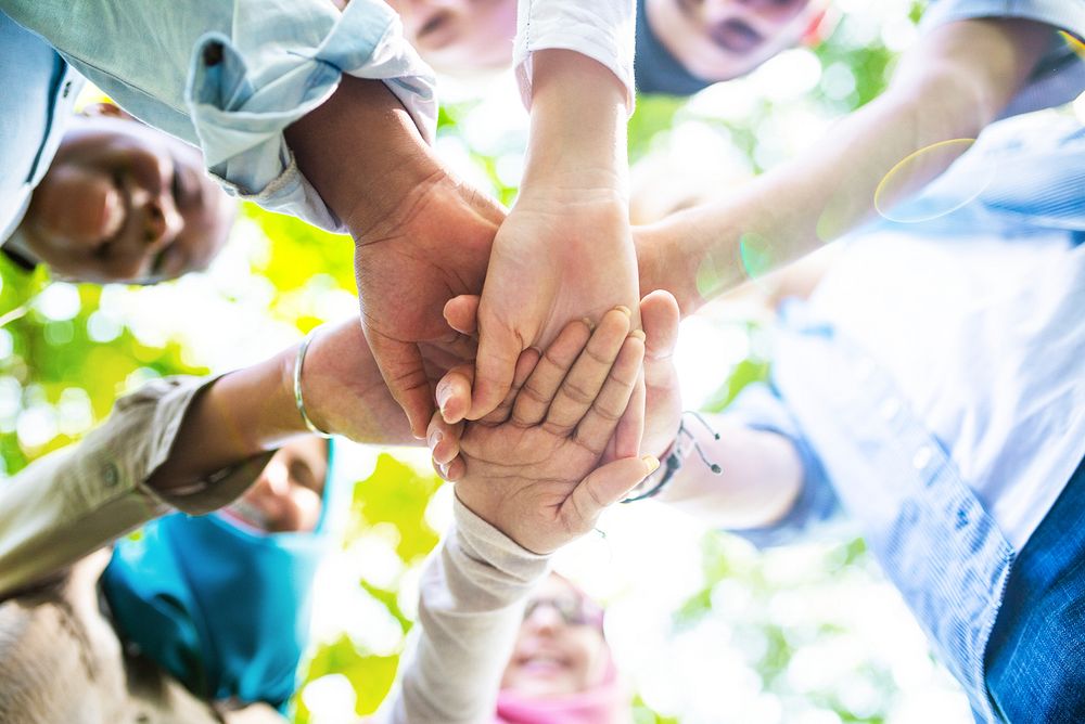 Diverse group of people joining hands in a circle, symbolizing teamwork and unity. Hands of different ethnicities and…