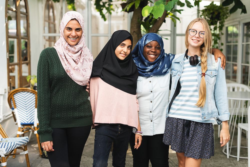 Four diverse women smiling, wearing casual clothing. Group of women includes different ethnicities, showcasing friendship…