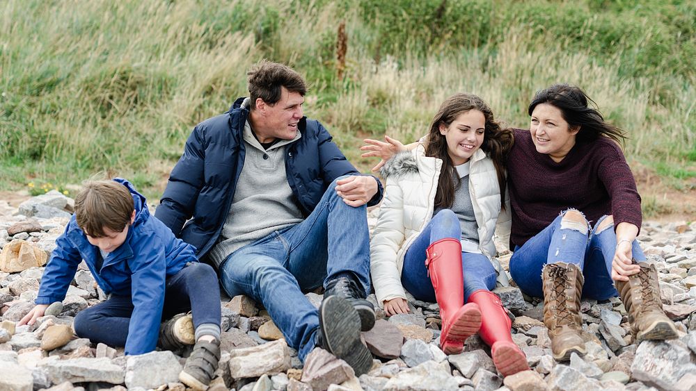 Family enjoy outdoors on rocky beach, sit and relax together. Parents with children enjoy travel outdoors, happy smile in…