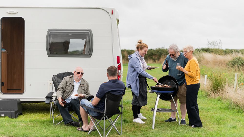 Diverse group of senior friends enjoying barbecue by a caravan. Outdoor gathering with friends. Relaxing near a caravan…