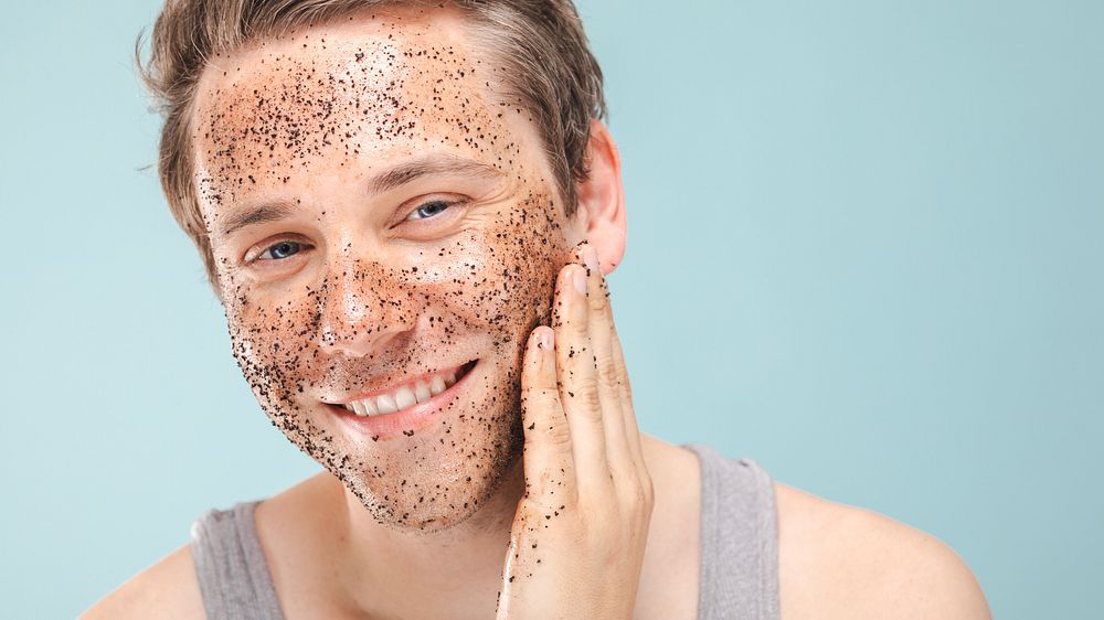 A man with a facial scrub smiles, applying exfoliating scrub. Skincare routine with facial scrub, exfoliating for healthy…