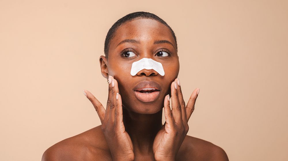 Black woman with short hair applies a nose strip, touching face. Skincare routine with a nose strip for clear skin. Neutral…