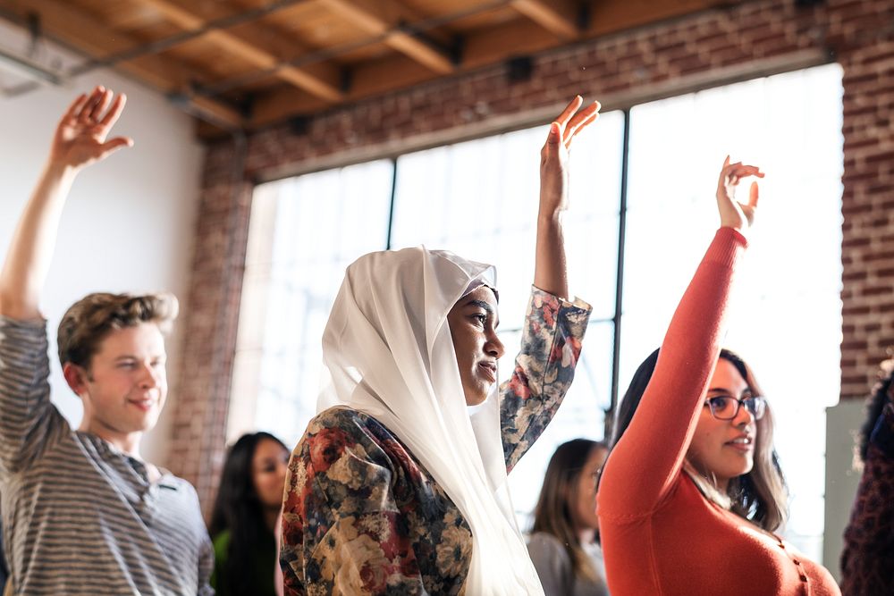 Woman in hijab and diverse group of people raising hands in a Seminar room setting, showing engagement and participation.…