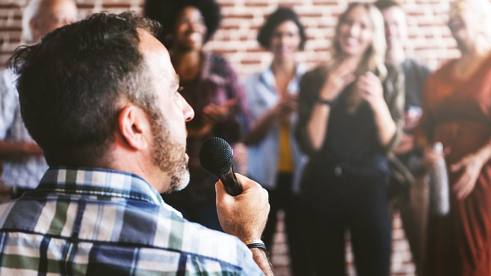 Man in wheelchair speaking to microphone in public with microphone, surrounded by diverse crowd. Joyful and supportive…