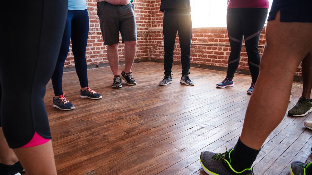 Group of people in athletic wear standing in a circle on wooden floor. Casual athletic shoes, diverse group, exercise…