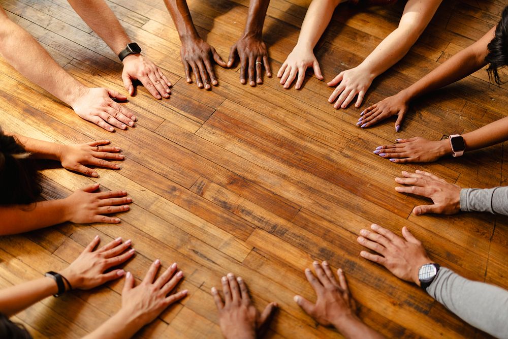 Diverse hands form a circle on a wooden floor. Unity, teamwork, and diversity. Hands circle team unity. Diverse people hands…