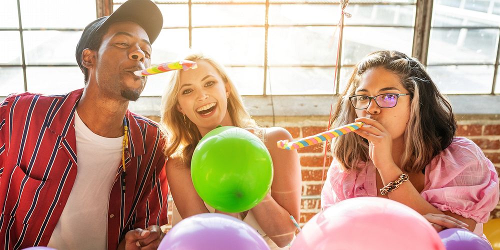 A joyful celebration scene featuring three friends all enjoying party hats, balloons, and festive noisemakers at a vibrant…