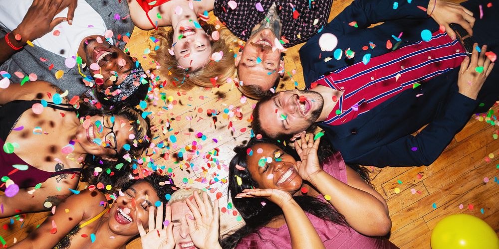 Group of diverse friends celebrating, lying on floor with confetti. Smiling, joyful, diverse group enjoying party. Happy…