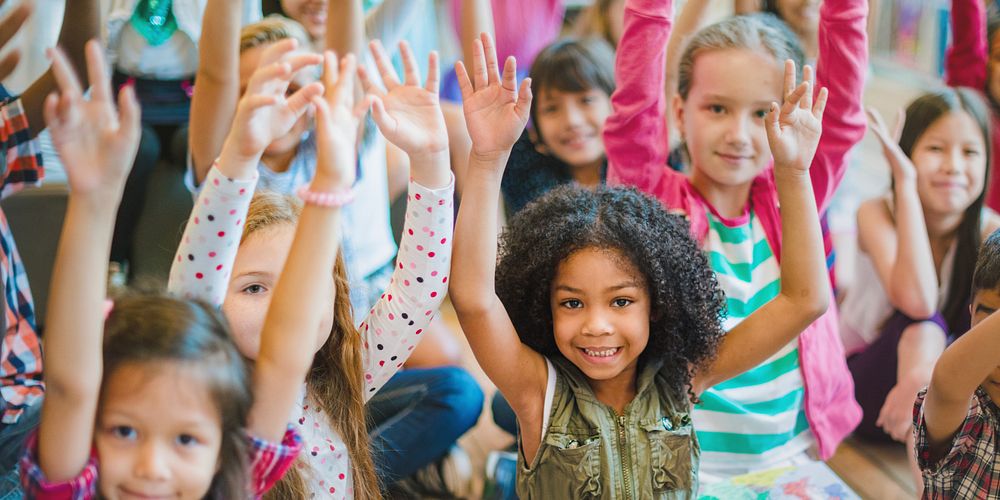 Group of diverse children raising hands in classroom. Smiling kids, eager to learn, show enthusiasm. Multicultural…