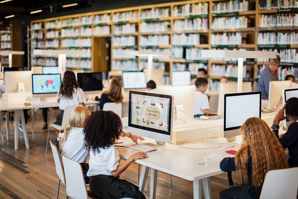 Students in library using computers. Diverse group of children learning. Library setting with computers. Kids engaged in…