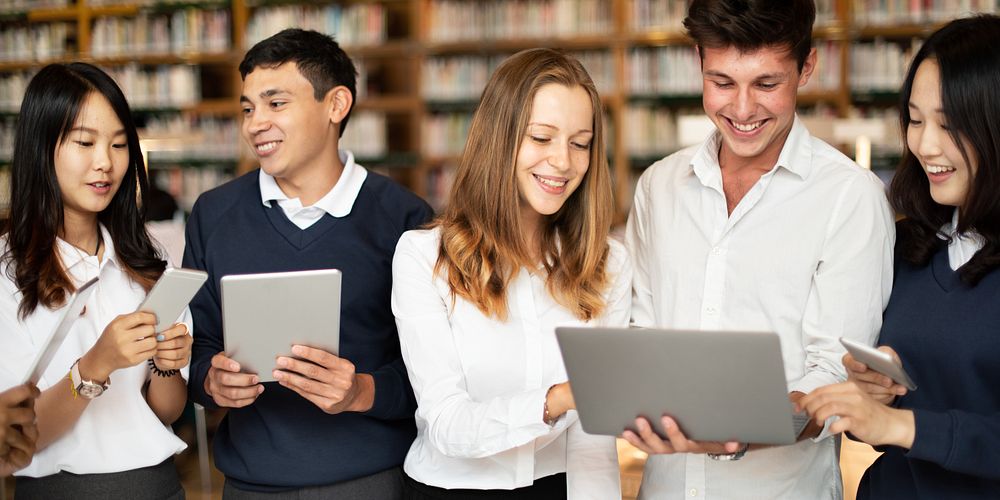 Diverse group of students in a library using tablets. Students engaged with technology. Diverse students learning with…