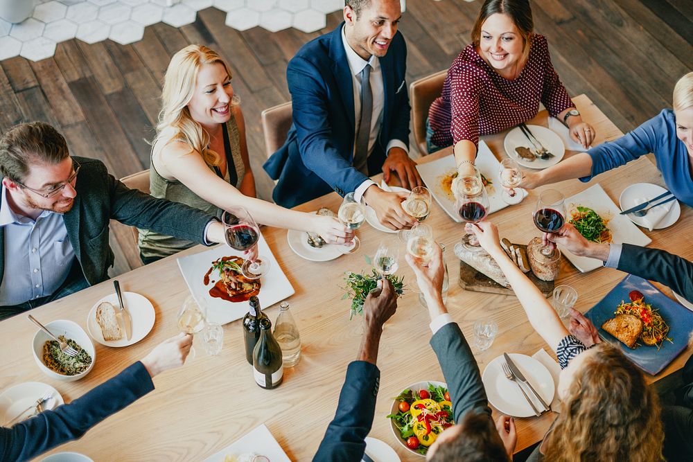 A diverse group of professionals, including men and women of various ethnicities, celebrate over a festive dinner. The…