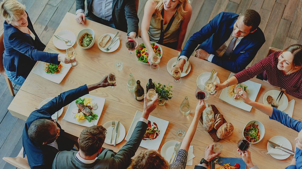 A diverse group of men and women celebrating at a dining table. The joyful gathering features toasts with drinks, delicious…