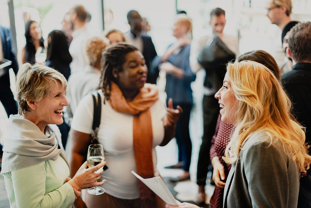 A diverse group of people, including women and men of various ethnicities, engage in lively conversation at a social event.…