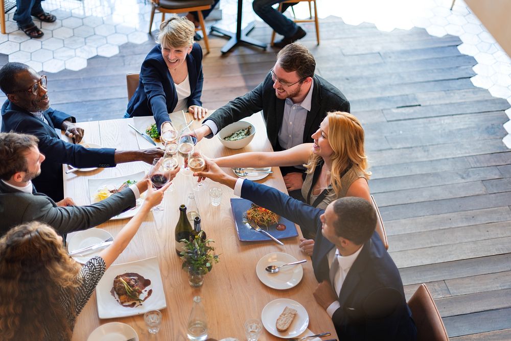 Group of diverse people enjoying meal together, toasting with wine glasses around a dining table, celebrating friendship and…