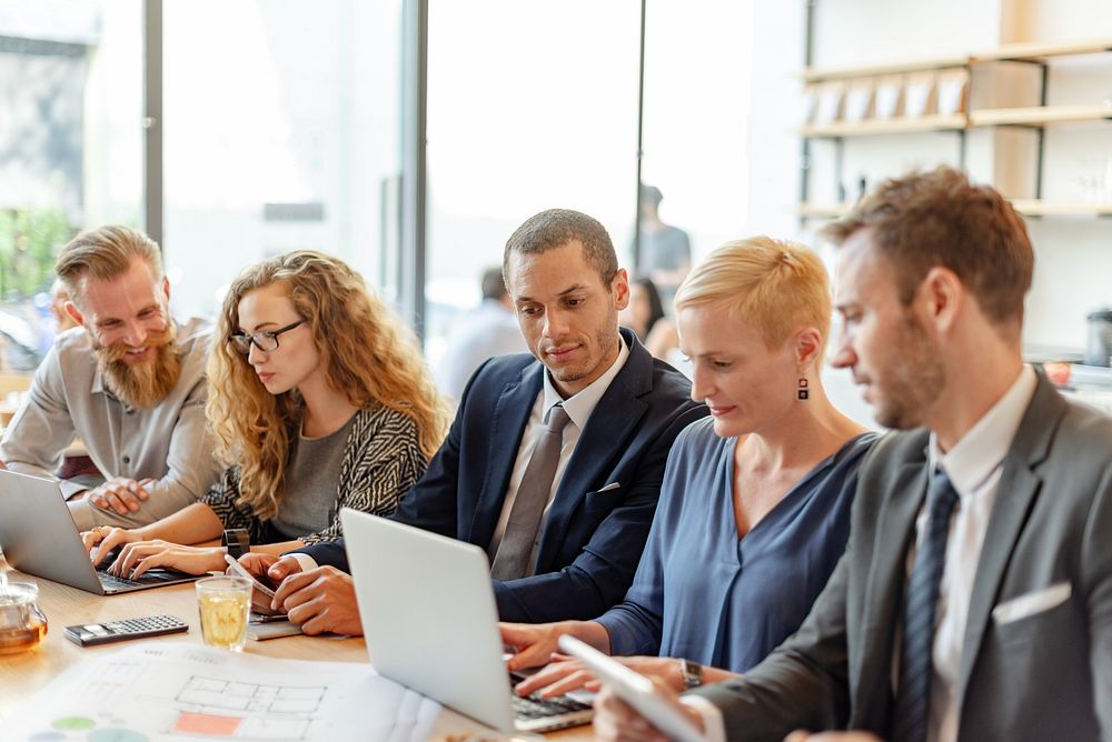 Diverse group of business people meeting together, using laptop and tablet in office. Mixed genders of business man and…