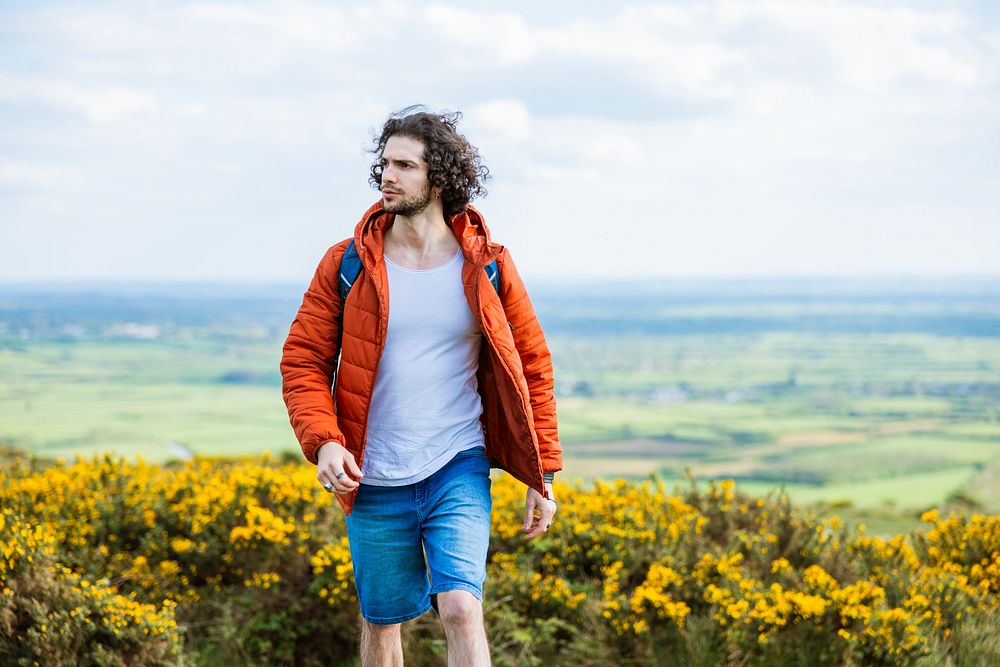 Man in orange jacket and blue shorts walking through a field. Outdoor adventure with a man enjoying nature. Bright orange…