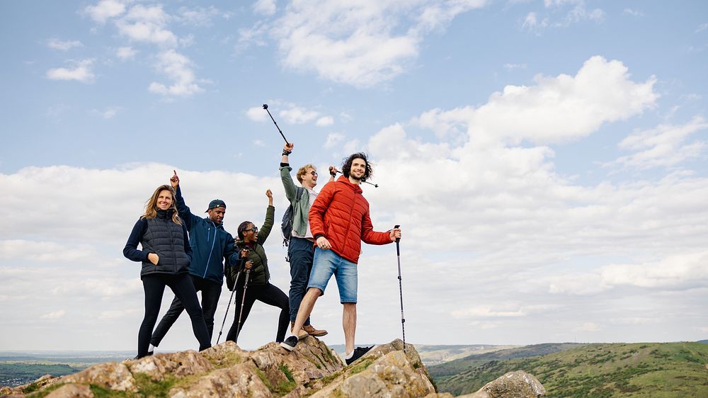 Group of hikers on a rocky peak, celebrating with trekking poles. Diverse group enjoying hiking, adventure, and nature.…