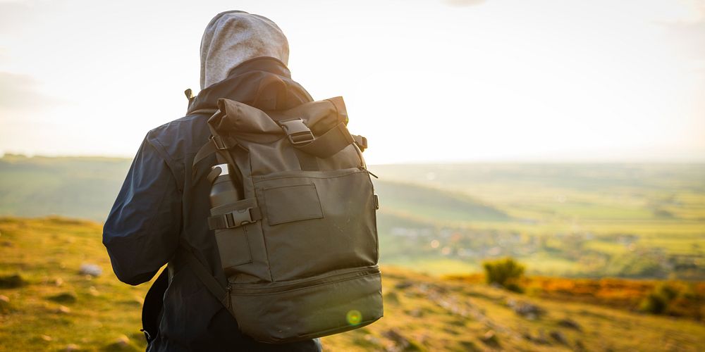 Person with backpack in outdoor setting, wearing a hoodie. Backpack and hoodie in focus. Outdoor adventure with backpack and…