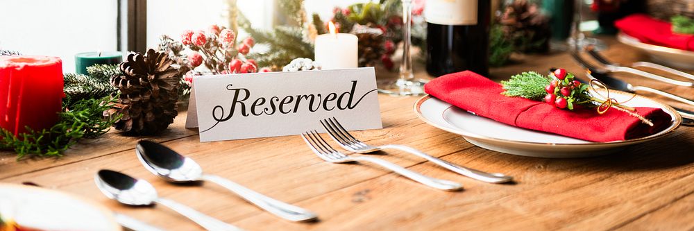 Festive table setting with reserved sign, red napkins, and candles. Holiday decor with reserved sign, pinecones, and red…