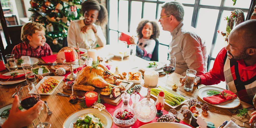 Festive family dinner with diverse group enjoying holiday meal. Christmas tree, turkey, and decorations create a joyful…