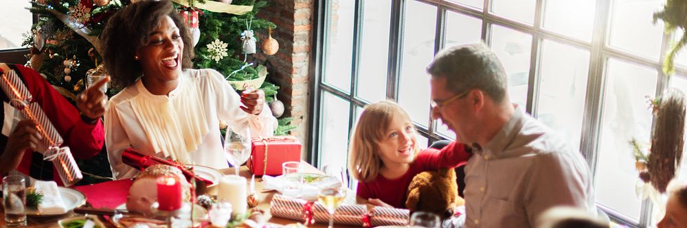 Festive family gathering around a Christmas table. Joyful celebration with diverse family. Christmas tree, gifts, and…