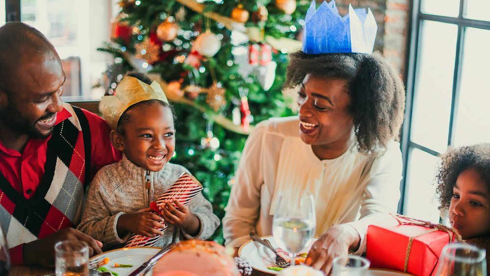 Family celebrating Christmas, exchanging gifts by a decorated tree. Smiling, joyful moments with festive hats. Warm…