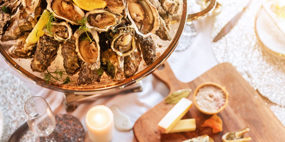 A platter of fresh oysters with lemon, surrounded by cheese and candles. Oysters and lemon, seafood feast. Oysters are the…