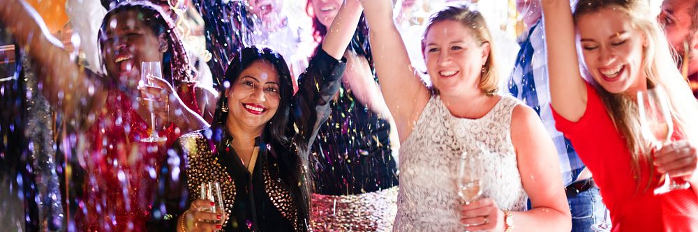 Group of diverse women celebrating at a party, smiling and raising glasses. Festive with confetti and joy. Women enjoying a…