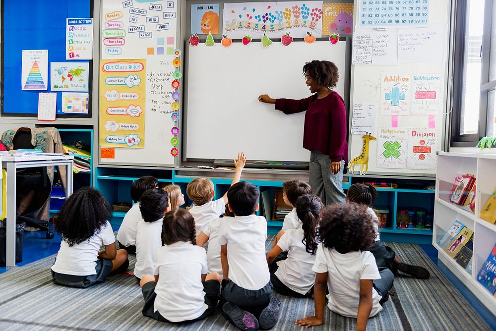 A teacher in a classroom with diverse children. The teacher, a Black woman, engages students. Classroom setting with…