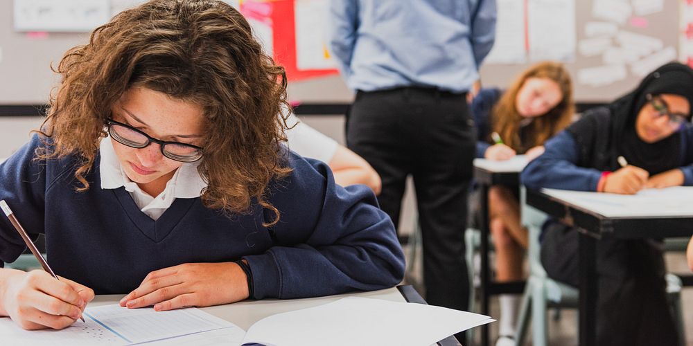 Students in a classroom taking a test. Focused students writing. Classroom setting with desks and papers. Diverse group…