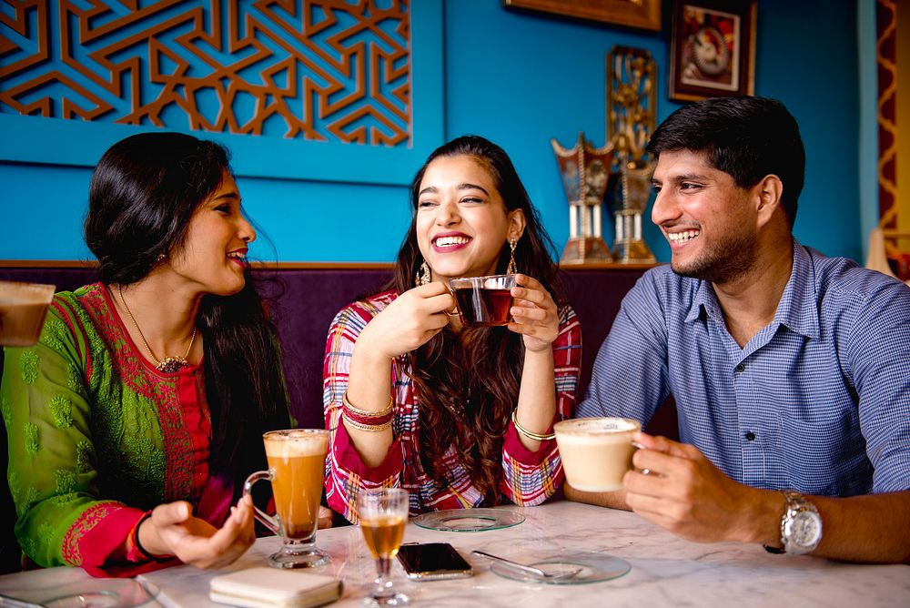 Three Indian people enjoying coffee and tea at a cafe. Smiling friends, diverse group, casual setting. Warm drinks, happy…