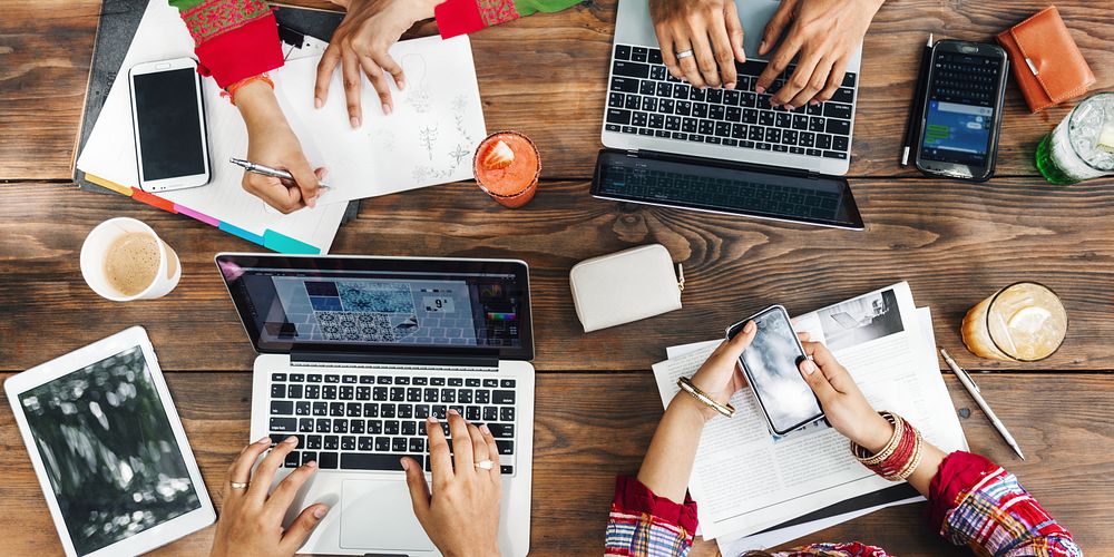 An Indian group of friends, collaborate at a wooden table, using laptops and smartphones for a productive brainstorming…