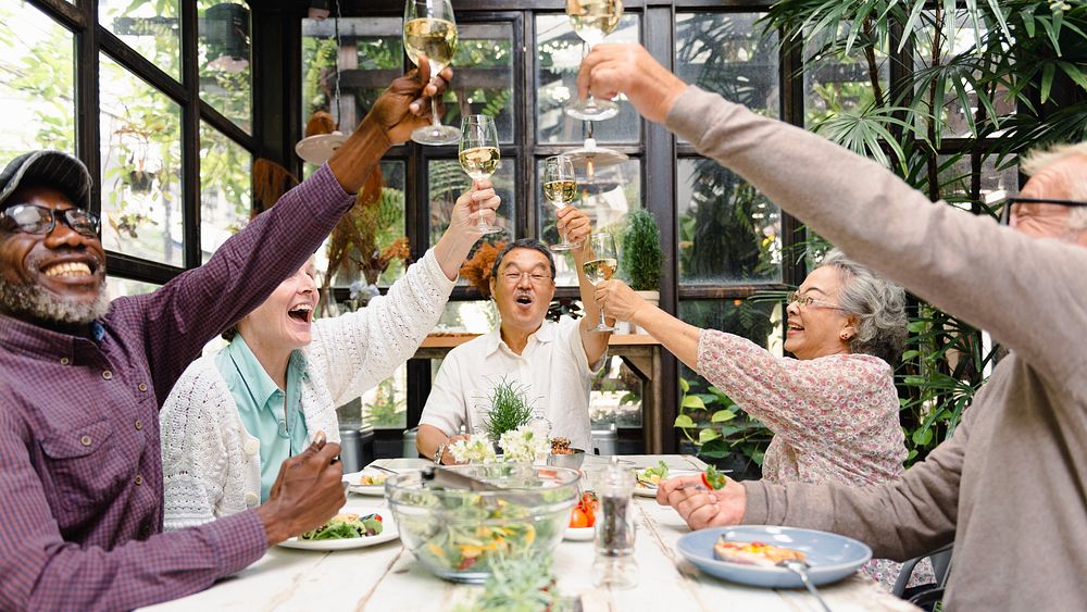 Group of diverse seniors enjoying a meal, raising glasses in celebration. Laughter and joy among elderly friends in a…