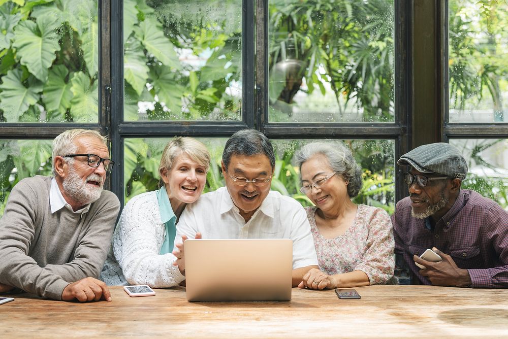 Diverse group of seniors enjoying time together. Seniors laughing, seniors using a laptop, seniors bonding. Happy seniors in…