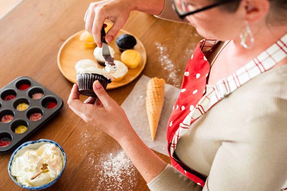 Woman decorating cupcakes with frosting. Cupcakes, frosting, and baking tools on a table. Baking cupcakes with care and…