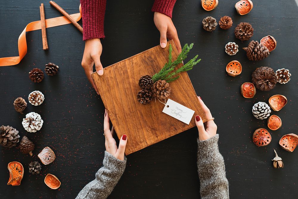 Hands exchanging a rustic gift box with pinecones, surrounded by autumn decor. Cozy, festive, and warm holiday atmosphere…