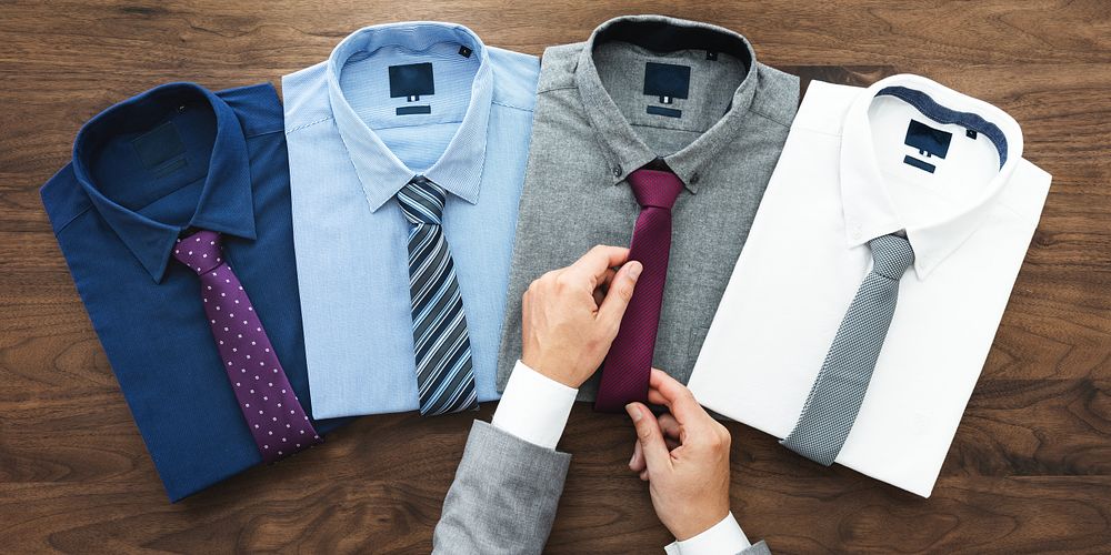 Four neatly folded dress shirts with ties on a wooden surface. A person adjusts a tie. Shirts and ties arranged in a row…