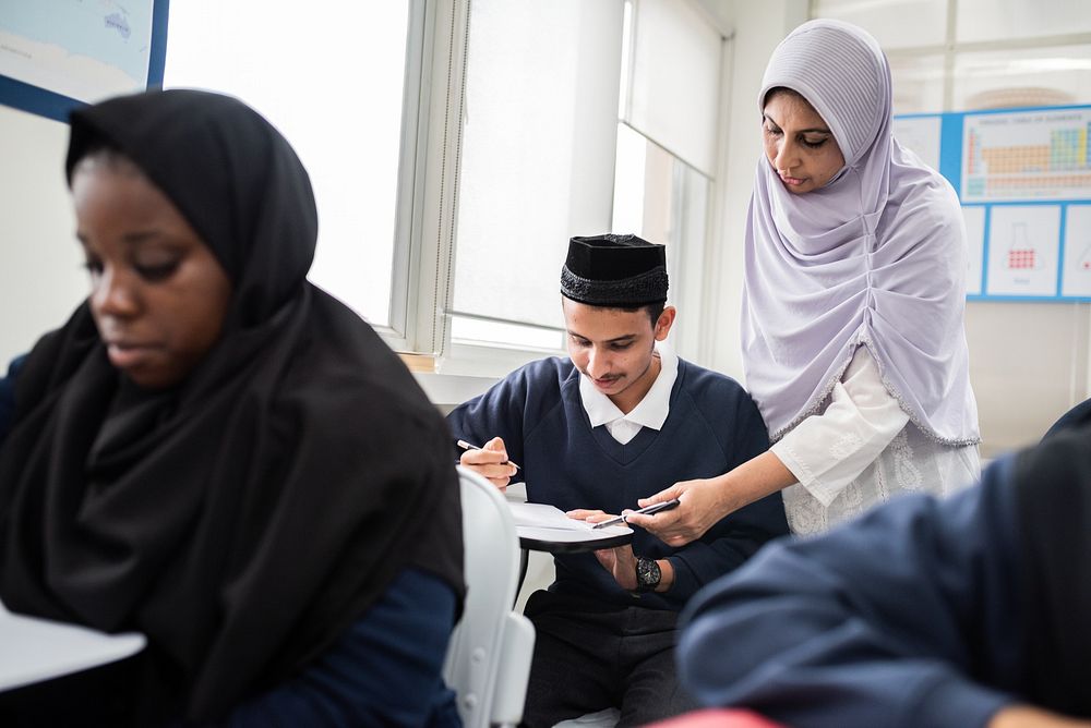 Muslim teacher in hijab assists students in classroom. Diverse classroom with attentive students. Education and learning…