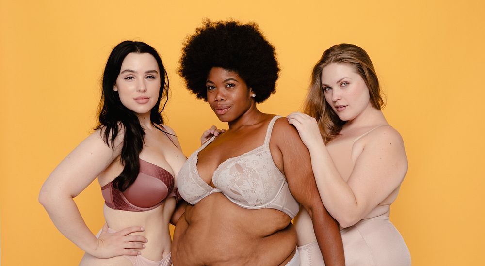 Three women in lingerie against a yellow background, showcasing body positivity and diversity. Embracing confidence and…