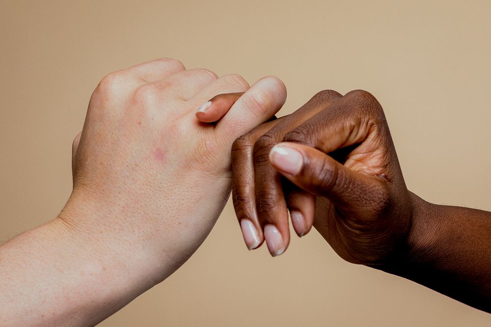 Two hands, one light-skinned and one dark-skinned, clasping together. Unity and diversity symbolized by hands. Hands showing…