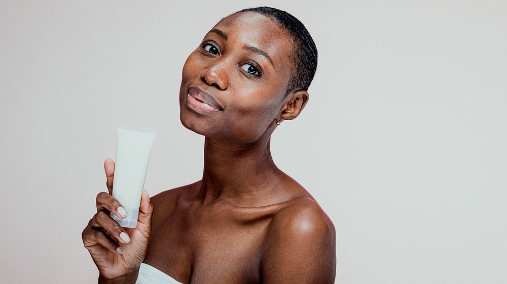 African woman holding skincare product, smiling. Skincare focus, beauty routine. African descent, glowing skin. Skincare…