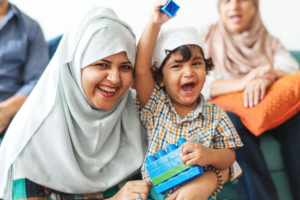 A joyful Muslim mother and her young son share a happy moment together. The smiling mother in a hijab and her excited son…