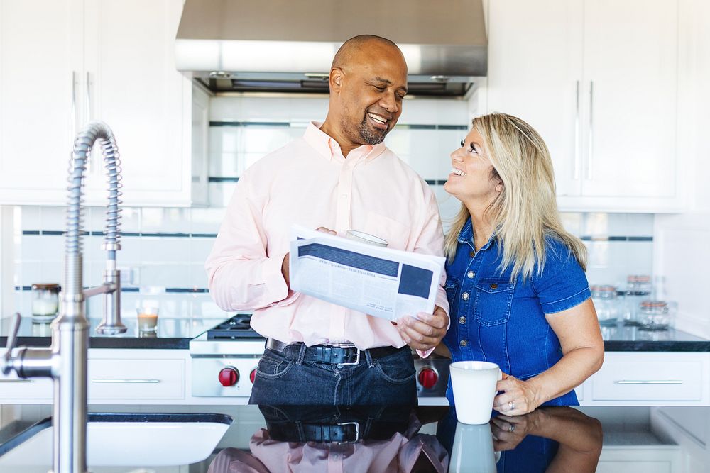 A couple in a modern kitchen, smiling and enjoying coffee. The man holds a tablet. Bright kitchen, happy couple, coffee…